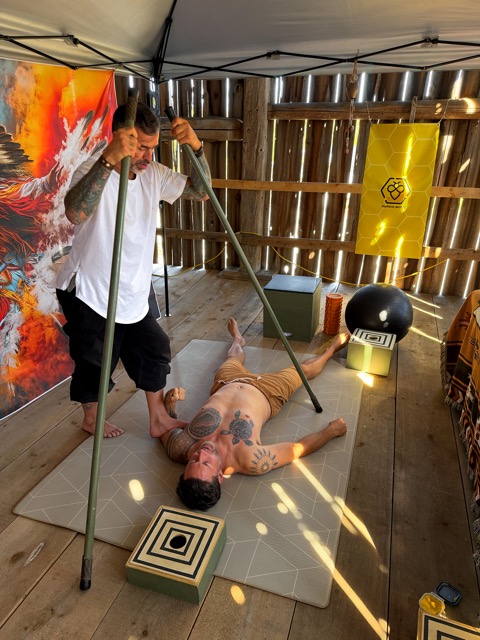 A Guide with two long poles working over a man lying on a mat, under the MyHive banner