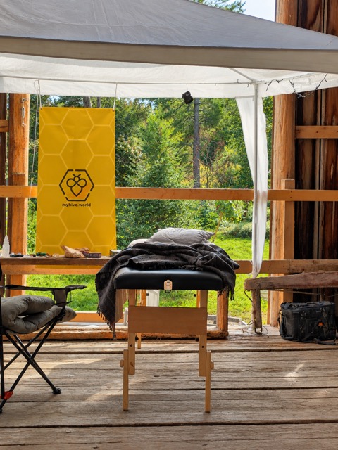 A massage table under a white tent, the MyHive banner and forest behind it